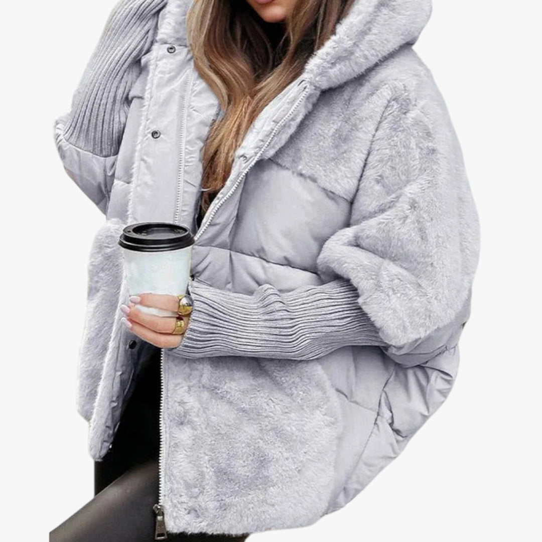 Person wearing a light gray puffer jacket holding a white cup with a black lid.