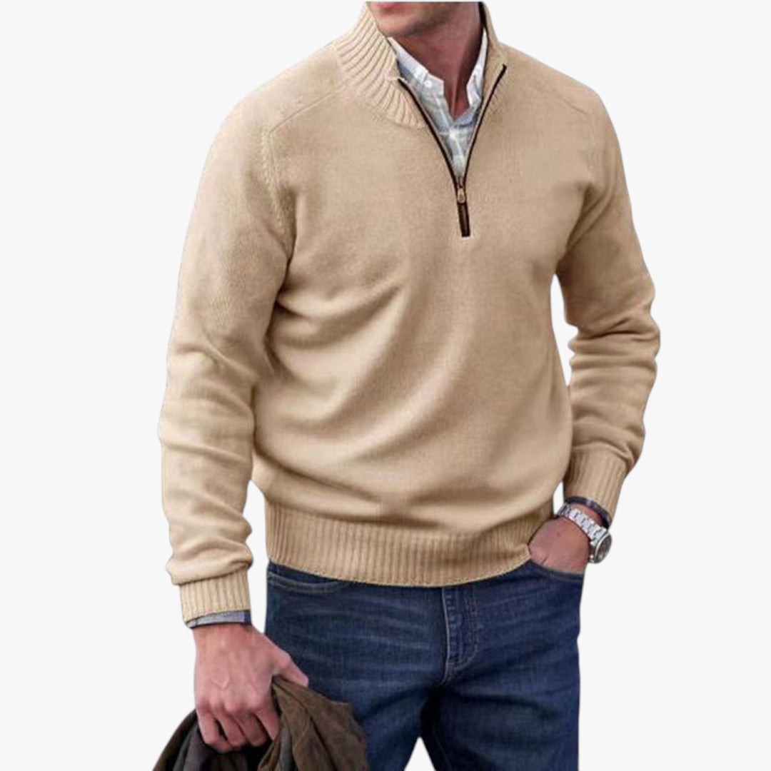 Man wearing a beige sweater with a zipper and blue jeans on a white background