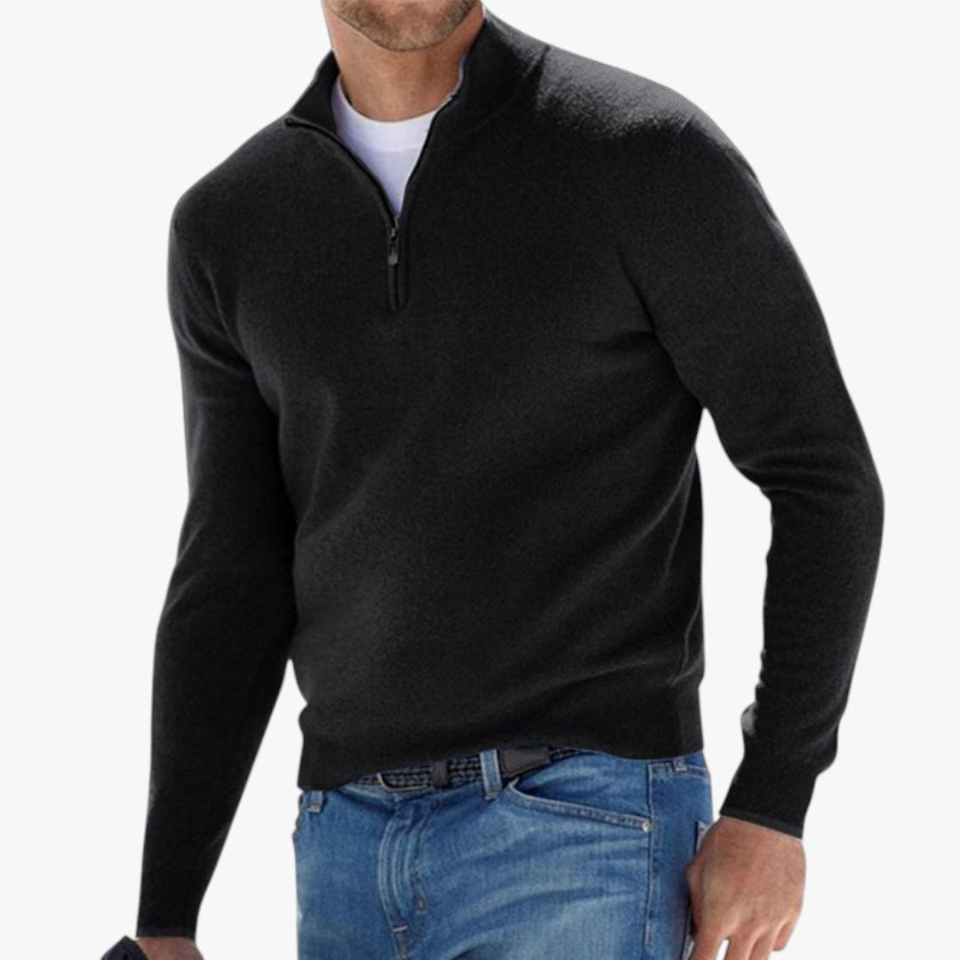 Man wearing a black quarter-zip sweater and blue jeans on a white background