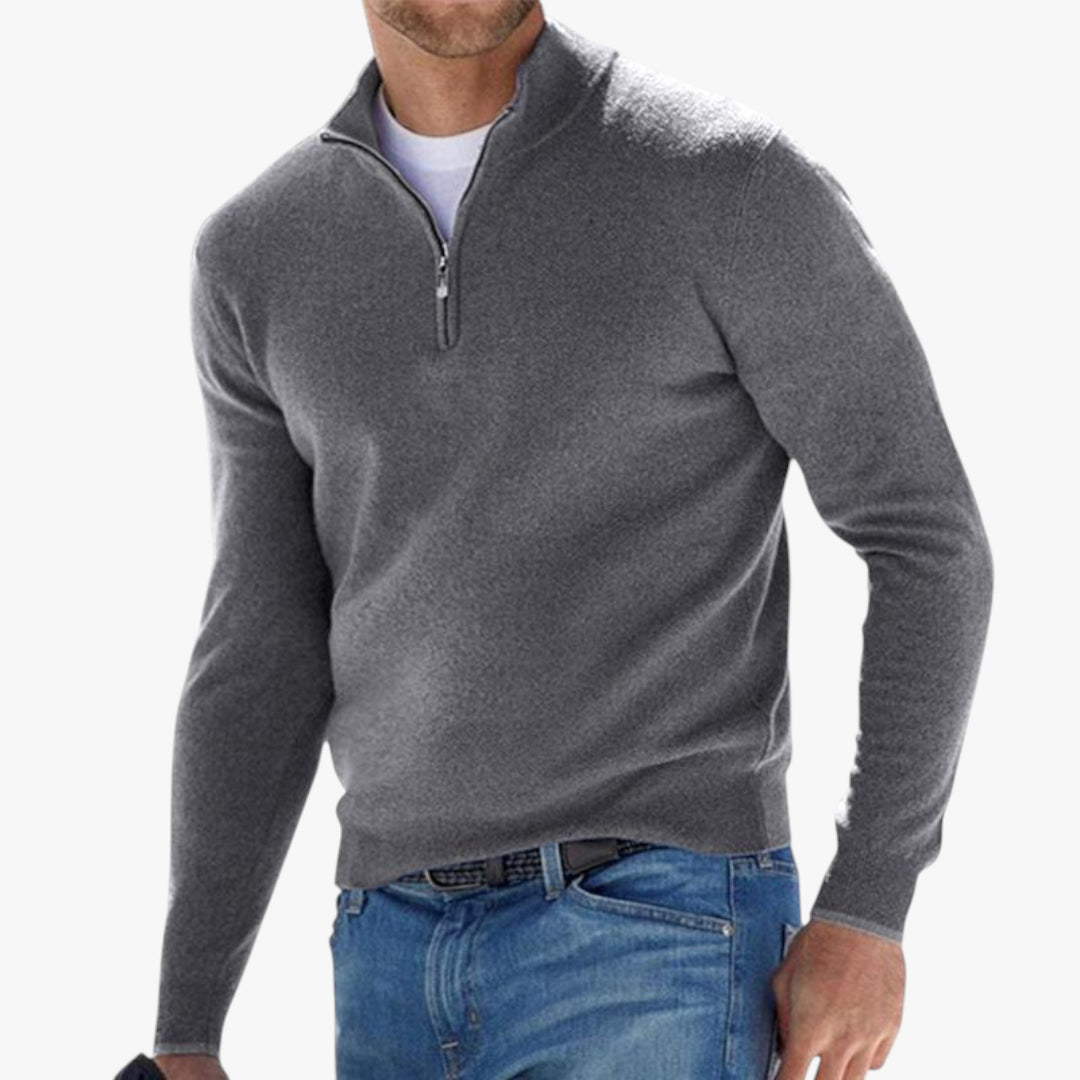 Man wearing a gray quarter-zip sweater and blue jeans on a white background